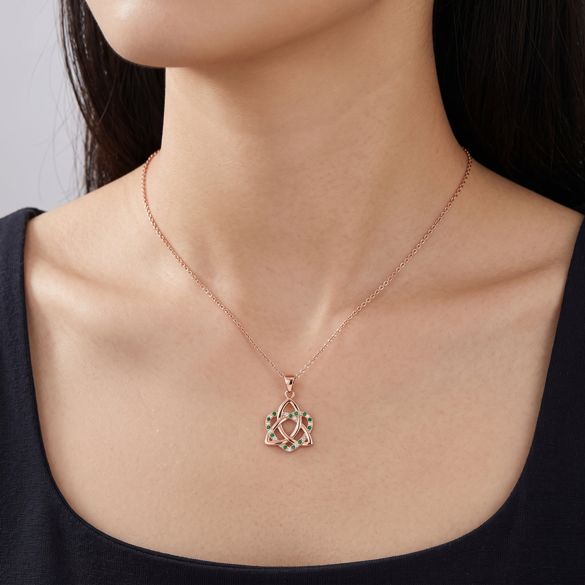 A close-up of a model wearing a delicate rose gold necklace with a geometric pendant featuring small green and white accents.